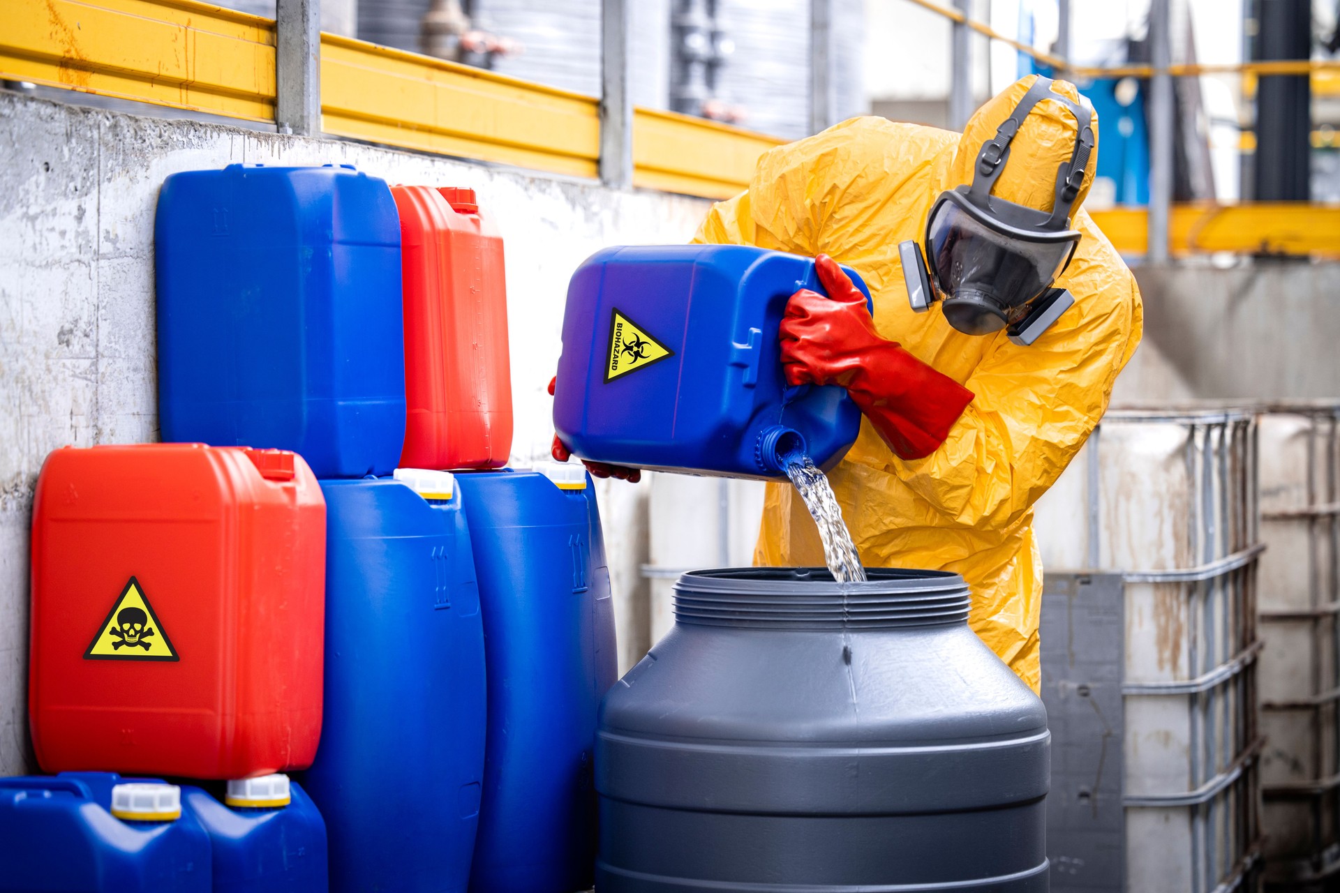 Factory worker wearing yellow protection suit and gas mask working in chemicals production plant handling acids.