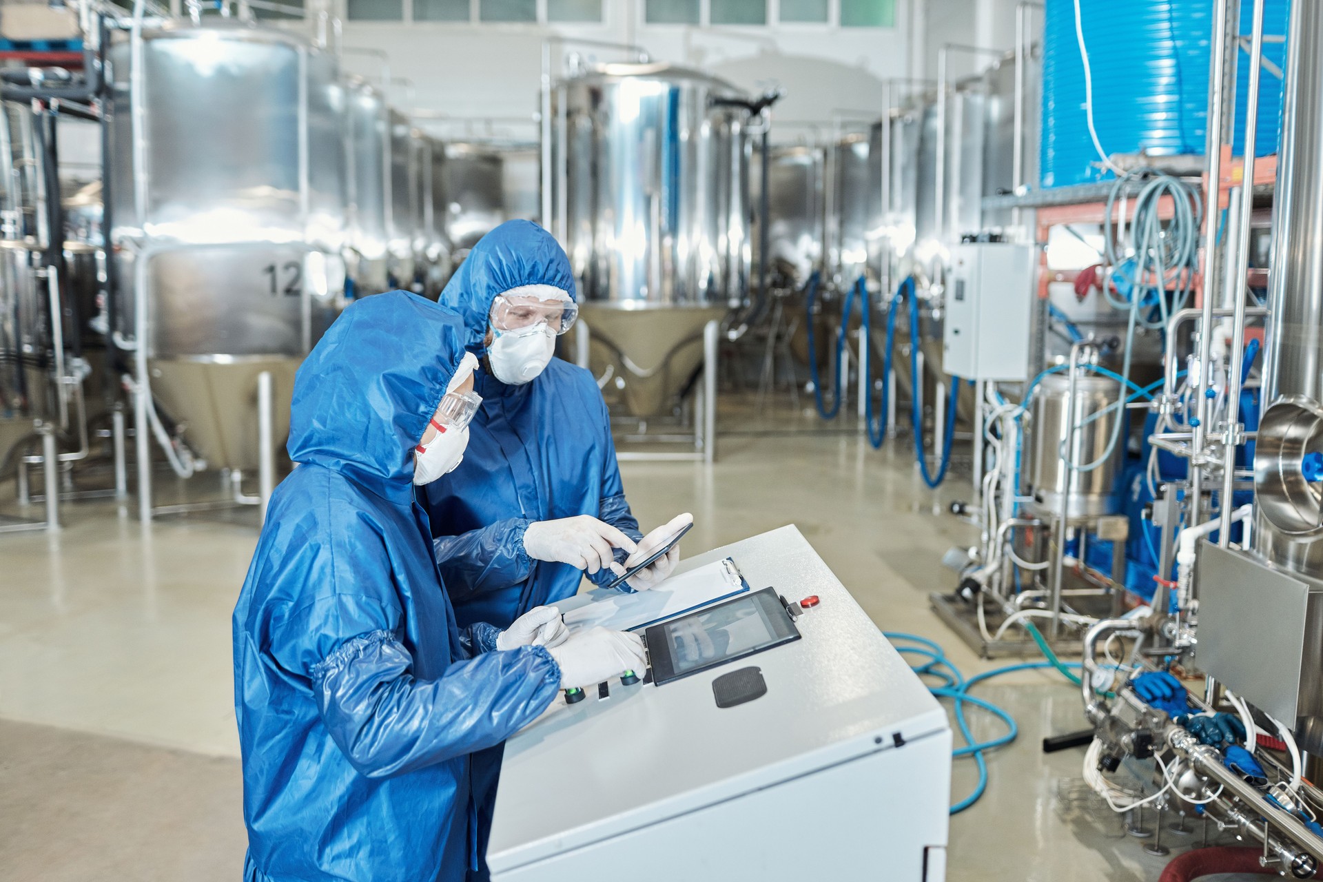 Two workers operating equipment at factory and using control panel